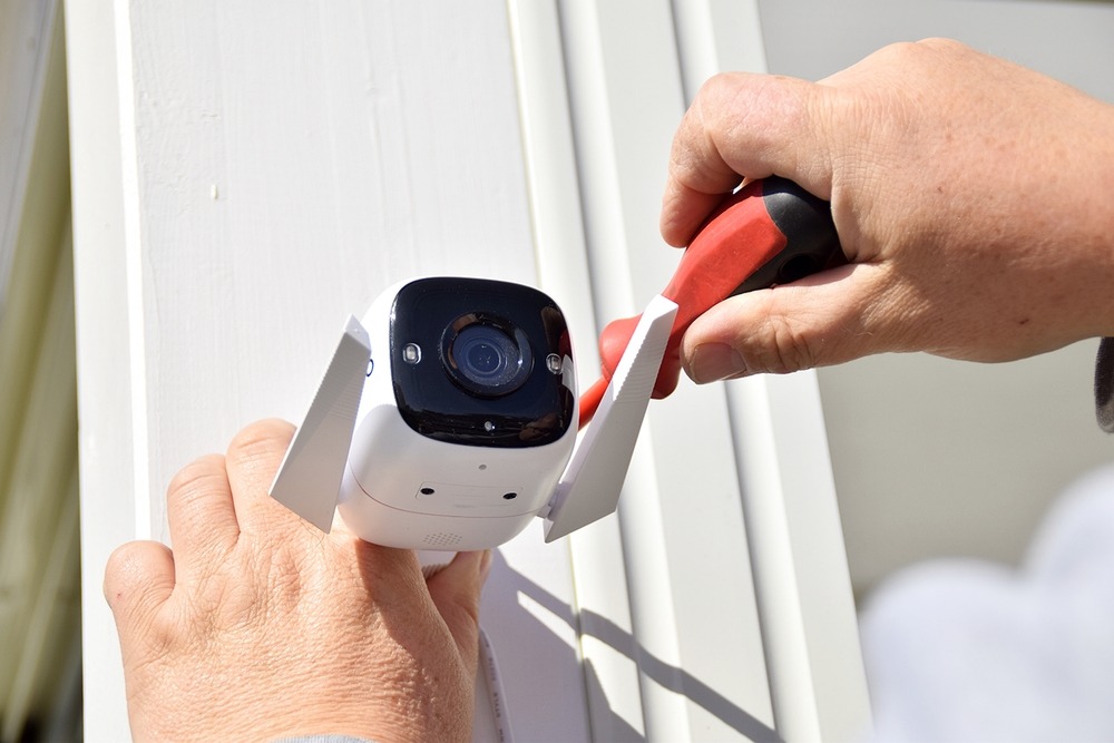 A,Man,Installs,A,Surveillance,Camera,Behind,The,House.,Security